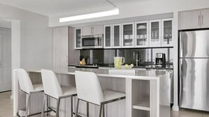 Eine moderne Küche mit einer zentralen Kochinsel, Barhocker, Edelstahlgeräten und einer Mikrowelle.