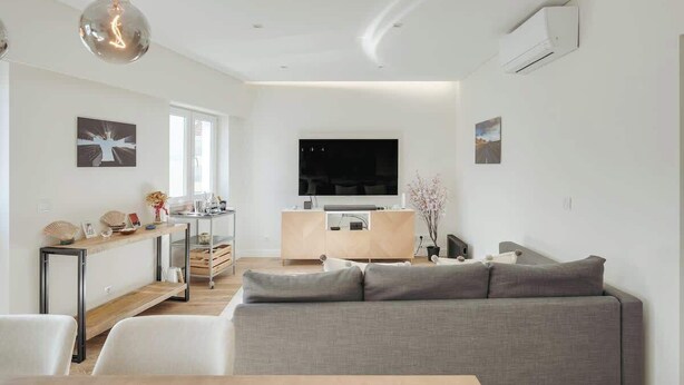 Un saló modern amb un sofà gris, una taula de centre de fusta i una televisió penjada a la paret.