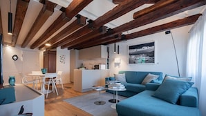 Ein modernes Wohnzimmer mit sichtbaren Holzbalken, einem blauen Sofa, einem Essbereich und einer Küche.