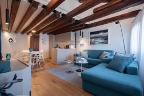 A modern living space with exposed wooden beams, a blue sofa, a dining area, and a kitchen.