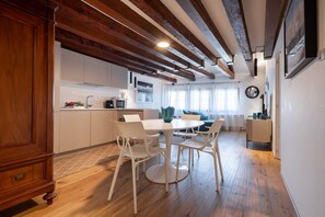 A modern kitchen with white cabinets, a dining area with white chairs, and exposed wooden beams on the ceiling. - Appartamento con due camere da letto matrimoniali a Dorsoduro molto luminoso (Venezia)