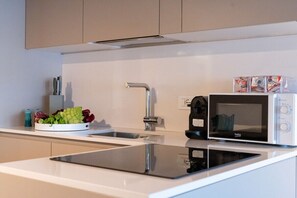 A modern kitchen with a built-in microwave, a sink, and a countertop with a cutting board and vegetables.