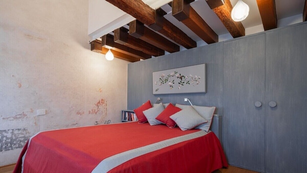 Ein Schlafzimmer mit einem Bett, Holzbalken, einer Deckenleuchte, einem an der Wand befestigten Kunstwerk und einem Kleiderschrank.