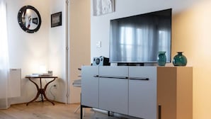 Ein modernes Zimmer mit einem weißen Schrank, einem runden Spiegel, einem kleinen Tisch und einem Flachbildfernseher.
