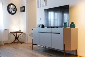 A modern room with a white cabinet, a round mirror, a small table, and a flat-screen TV.