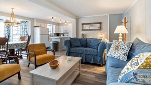 A spacious living room with a blue sofa, a wooden coffee table, and a dining area with a patterned tablecloth.