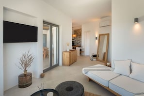 Un salon moderne avec un canapé, une table basse et une cheminée. On aperçoit à l’arrière-plan un coin cuisine avec un mur en pierre et une table à manger.