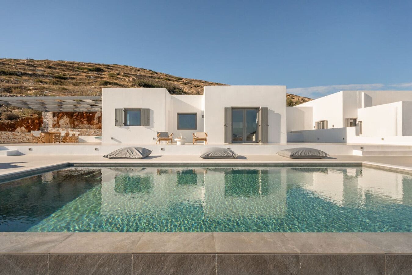 Un espace moderne aménagé autour d’une piscine, avec une eau cristalline, des bâtiments blancs et des espaces de détente en plein air.