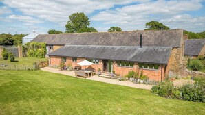 A traditional brick house with a sloped roof, a patio with outdoor furniture, and a well-maintained lawn. - Battys Barn at Moorbath Farm (Bridport)