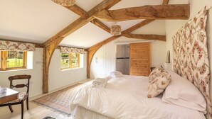 A bedroom with a large bed, wooden beams, a window, a chair, and a small table. - Battys Barn at Moorbath Farm (Bridport)