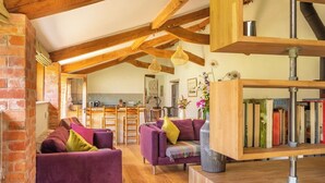 A cozy living room with a fireplace, a kitchen in the background, and a bookshelf. - Battys Barn at Moorbath Farm (Bridport)