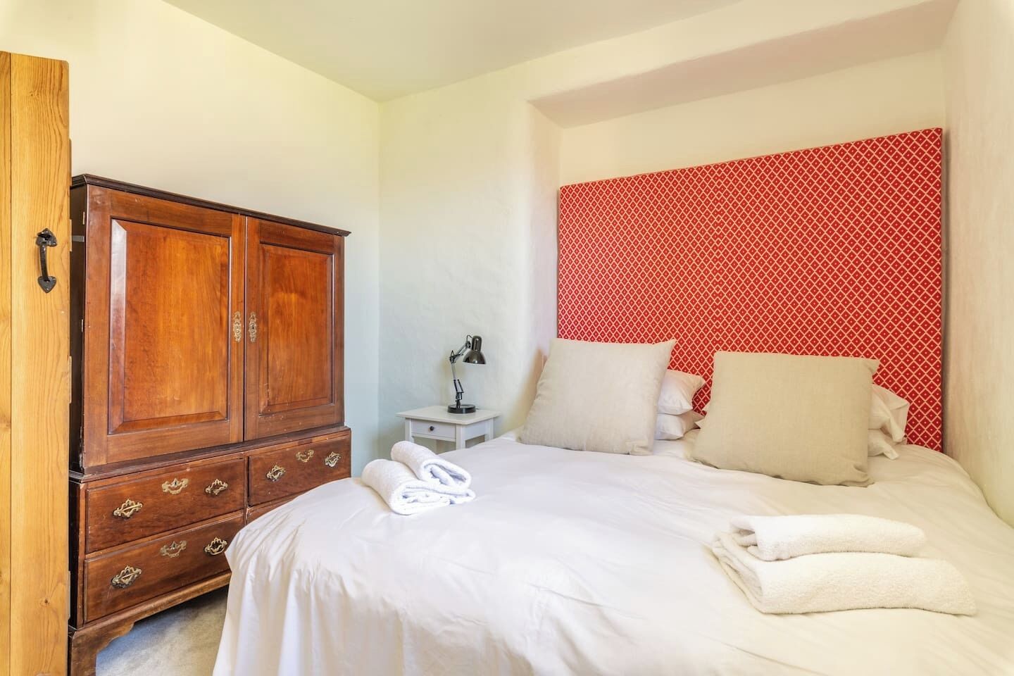 Een slaapkamer met een houten garderobe, een nachtkastje met een lamp, en een bed met witte lakens en kussens.