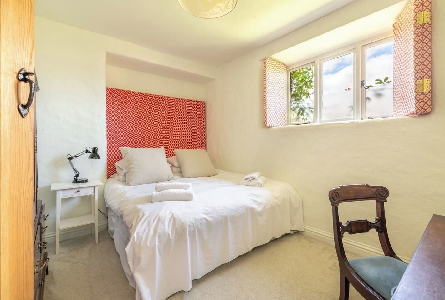 A bedroom with a bed, a desk, a chair, and a window with curtains.