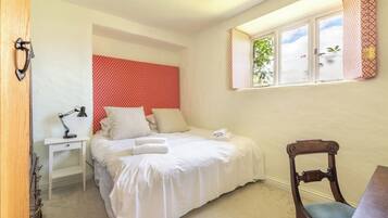 A bedroom with a bed, a desk, a chair, and a window with curtains.