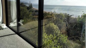 Vista desde una habitación con ventanas amplias que dan a una playa y al océano.