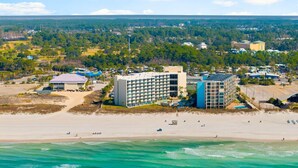 A coastal hotel with multiple buildings, a beach, and a view of the surrounding landscape.