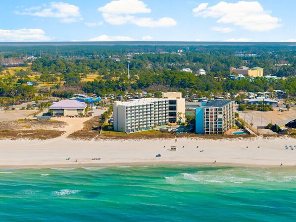 A coastal hotel with multiple buildings, a beach, and a view of the surrounding landscape.