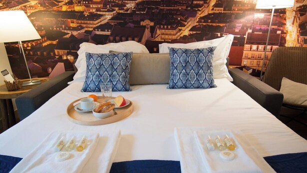 A hotel room with a bed, two pillows, a tray with breakfast, and towels. - Vibrant Central Studio (Lisbon)