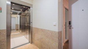 A modern elevator with a glass door, a marble-tiled floor, and a wall-mounted light switch. - Vibrant Central Studio (Lisbon)