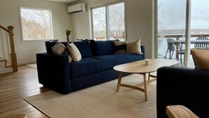 Ett modernt vardagsrum med en blå soffa, ett träbord och utsikt över naturen genom stora fönster.