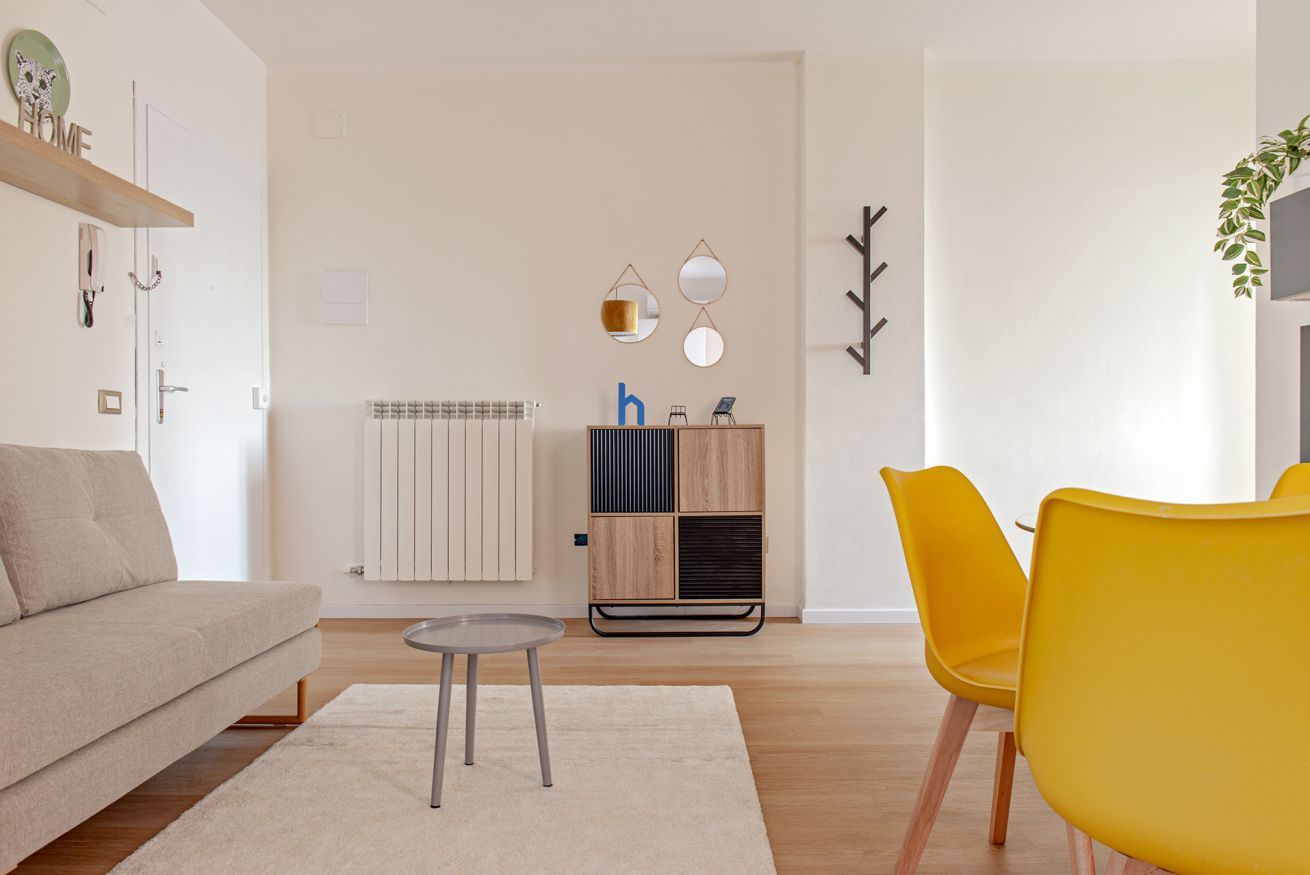 A modern living room with a sofa, a small round table, and two yellow chairs.