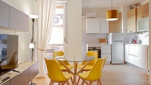 A modern kitchen with white cabinets, a built-in oven, and a refrigerator. There is a dining area with a glass table and yellow chairs. - Our newly renovated property is designed to offer you maximum comfort. The bright and spacious bedroom is equipped with a comfortable double bed, ideal for a regenerating sleep. The living room is perfect for relaxing, with a sofa that turns into a bed t (Pisa)
