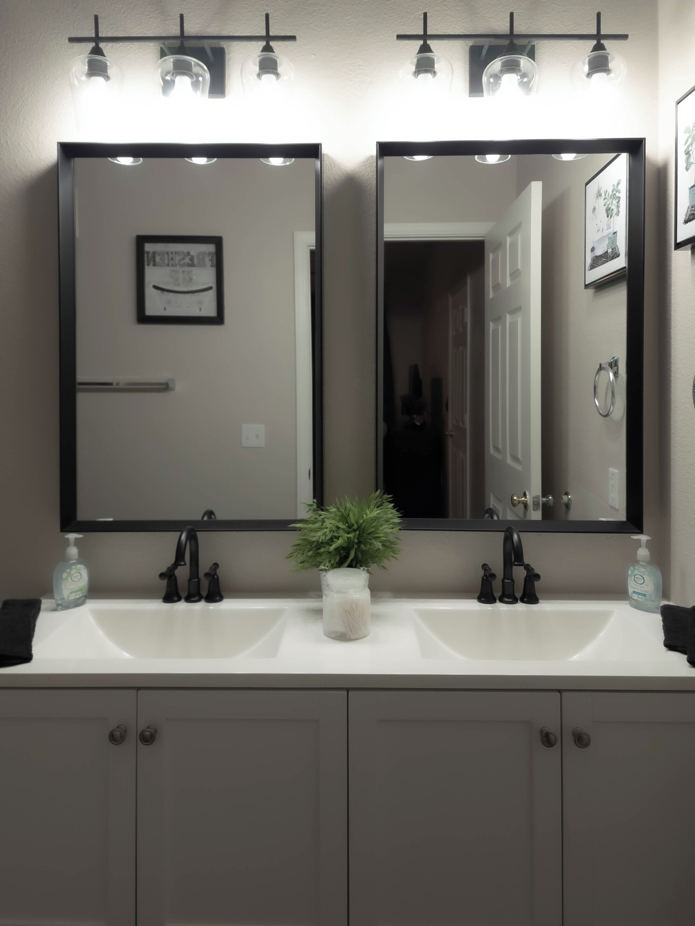 A bathroom with two mirrors, a sink, a plant, and a door.