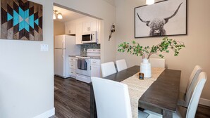 A modern kitchen with white cabinets, a microwave, and a stove. There is a dining table with white chairs and a vase with green plants. - 4BR Mountain Retreat , Fireplace, Deck with Views, RMNP (Fraser)