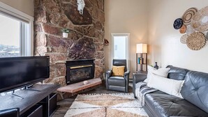 A living room with a stone fireplace, a flat-screen TV, a leather sofa, and a decorative wall. - 4BR Mountain Retreat , Fireplace, Deck with Views, RMNP (Fraser)