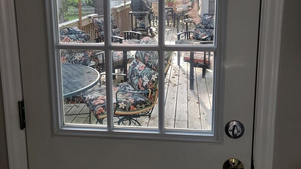 A white door with a window, through which a patio area with outdoor furniture and a wooden deck is visible. - Charming 1-bedroom apartment in cool Garner, minutes from Raleigh (Garner)