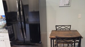 A black Whirlpool refrigerator next to a wooden dining table with a chair. - Charming 1-bedroom apartment in cool Garner, minutes from Raleigh (Garner)