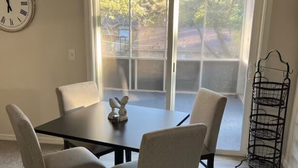 A dining area with a dark wooden table and four chairs, a wall clock, and a window with a view of trees. - Lazy E Country Cozy in Edmond Oklahoma (Edmond)