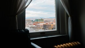 Huone, jossa on ikkuna, valkoiset verhot, patteri ja tuoli.
