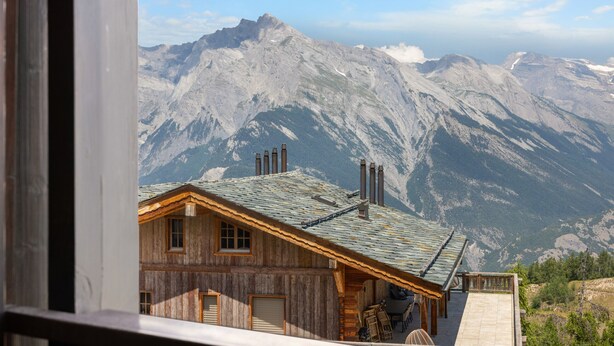A wooden cabin with a sloped roof, a chimney, and a view of a mountain range. - Eden Roc 6 - 4 pers - près des pistes (Haute-Nendaz)