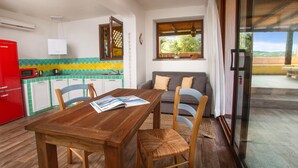Ein Holzespeisesaal mit Stühlen, ein roter Kühlschrank, eine Küchenzeile mit einer Mikrowelle und Blick durch eine Glastür auf eine Außenpatio.