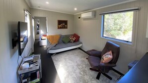Un espace de vie compact comprenant un canapé, un fauteuil inclinable, un téléviseur à écran plat et une petite table avec un plateau.