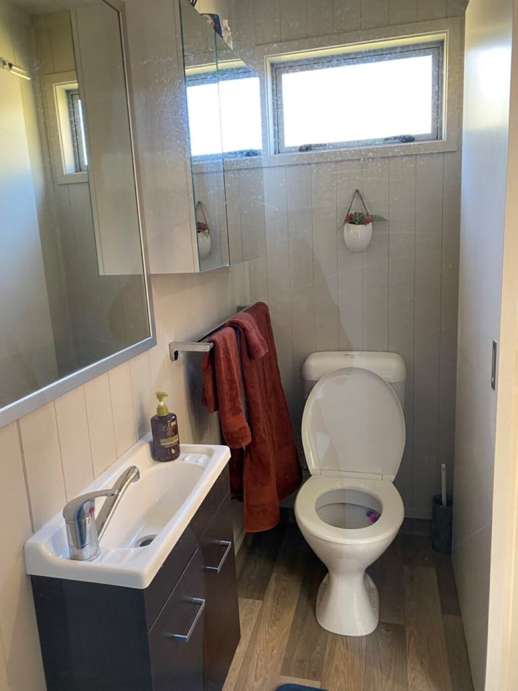 A compact bathroom with a white toilet, a sink with a mirror above it, and a window above the toilet.