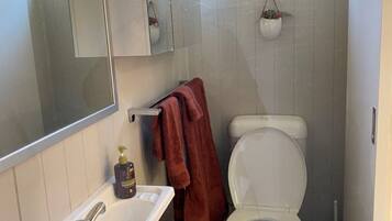 A compact bathroom with a white toilet, a sink with a mirror above it, and a window above the toilet.