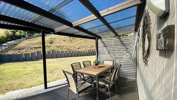Une terrasse extérieure avec une table et des chaises en bois, un toit en métal et une vue sur une zone herbeuse.