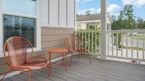 A covered porch with two wicker chairs and a small table, overlooking a residential street.