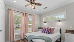 A bedroom with a bed, wooden flooring, a ceiling fan, and a window with blinds.