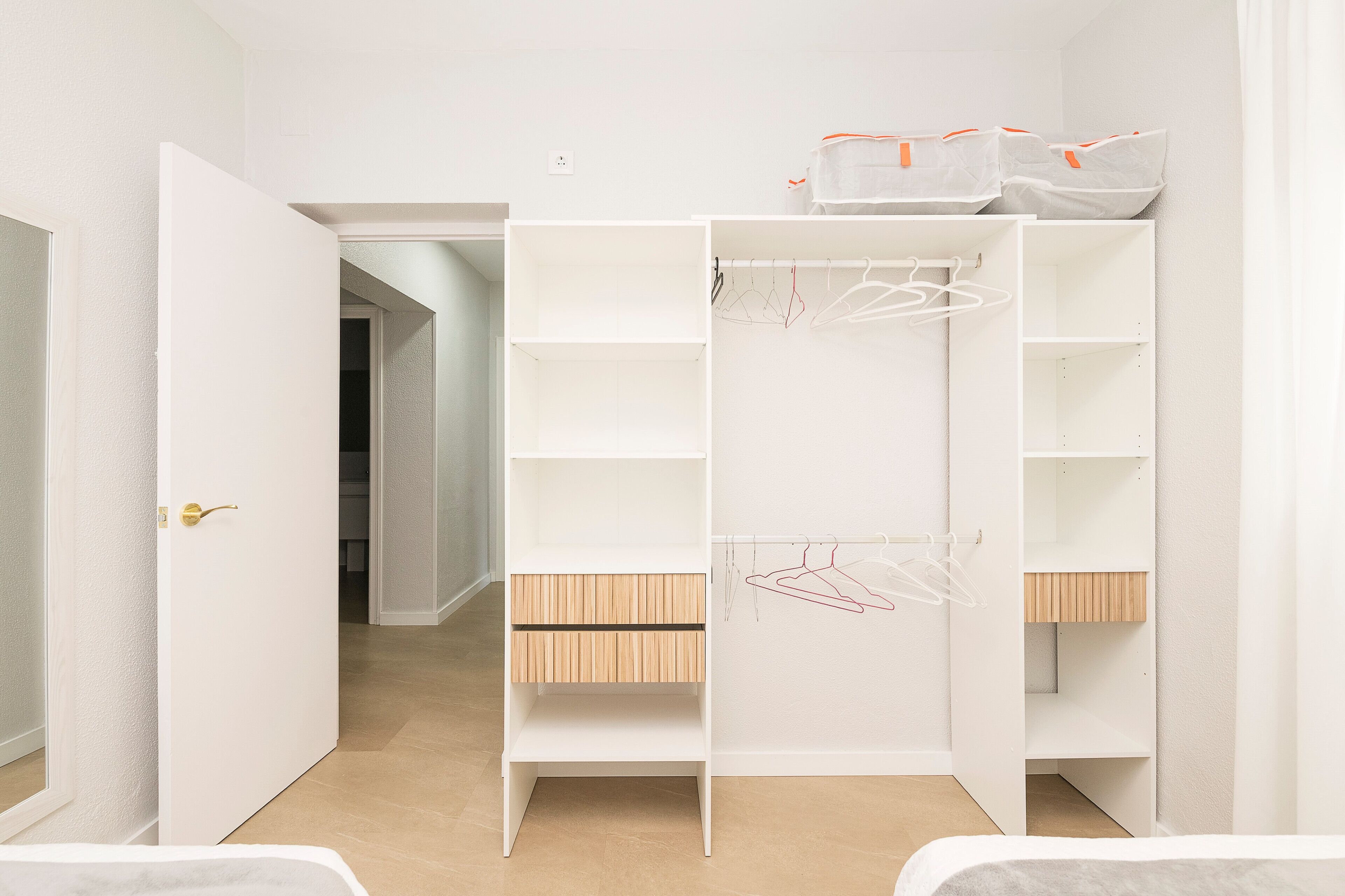 Ein begehbarer Kleiderschrank mit mehreren Regalen und Ablageflächen, einer Holzbank und einer Tür mit goldener Klinke.