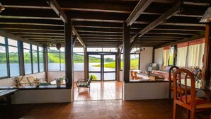 A spacious room with a view of a lake, a wooden ceiling, and a dining area with chairs and a table.