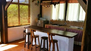 A kitchen with a wooden bar stool area, a window with blinds, and a hanging light fixture.