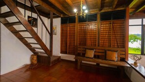 A wooden staircase leading to a balcony with a view of greenery. A wooden bench with cushions is placed against the wall.