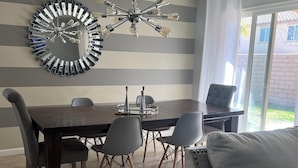 A dining area with a large round table, six chairs, a modern chandelier, and a large mirror on the wall. - Charming 3-bedroom house with AC, WiFi in fantastic Coachella (Coachella)
