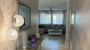 A hallway with a glass console table, a floor lamp, and a mirror. There is a living room area with a sofa, a coffee table, and a ceiling fan. - Charming 3-bedroom house with AC, WiFi in fantastic Coachella (Coachella)