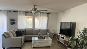 A living room with a sofa, coffee table, TV, ceiling fan, and potted plants. - Charming 3-bedroom house with AC, WiFi in fantastic Coachella (Coachella)