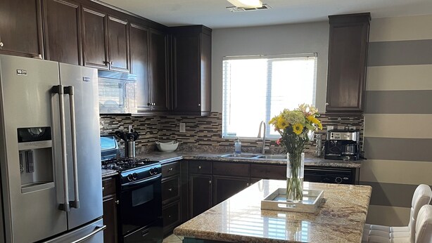 A modern kitchen with dark cabinetry, stainless steel appliances, a granite countertop island, and a window providing natural light. - Charming 3-bedroom house with AC, WiFi in fantastic Coachella (Coachella)