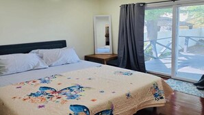 A bedroom with a bed, a nightstand, a mirror, and a view of the outdoors through a sliding glass door.